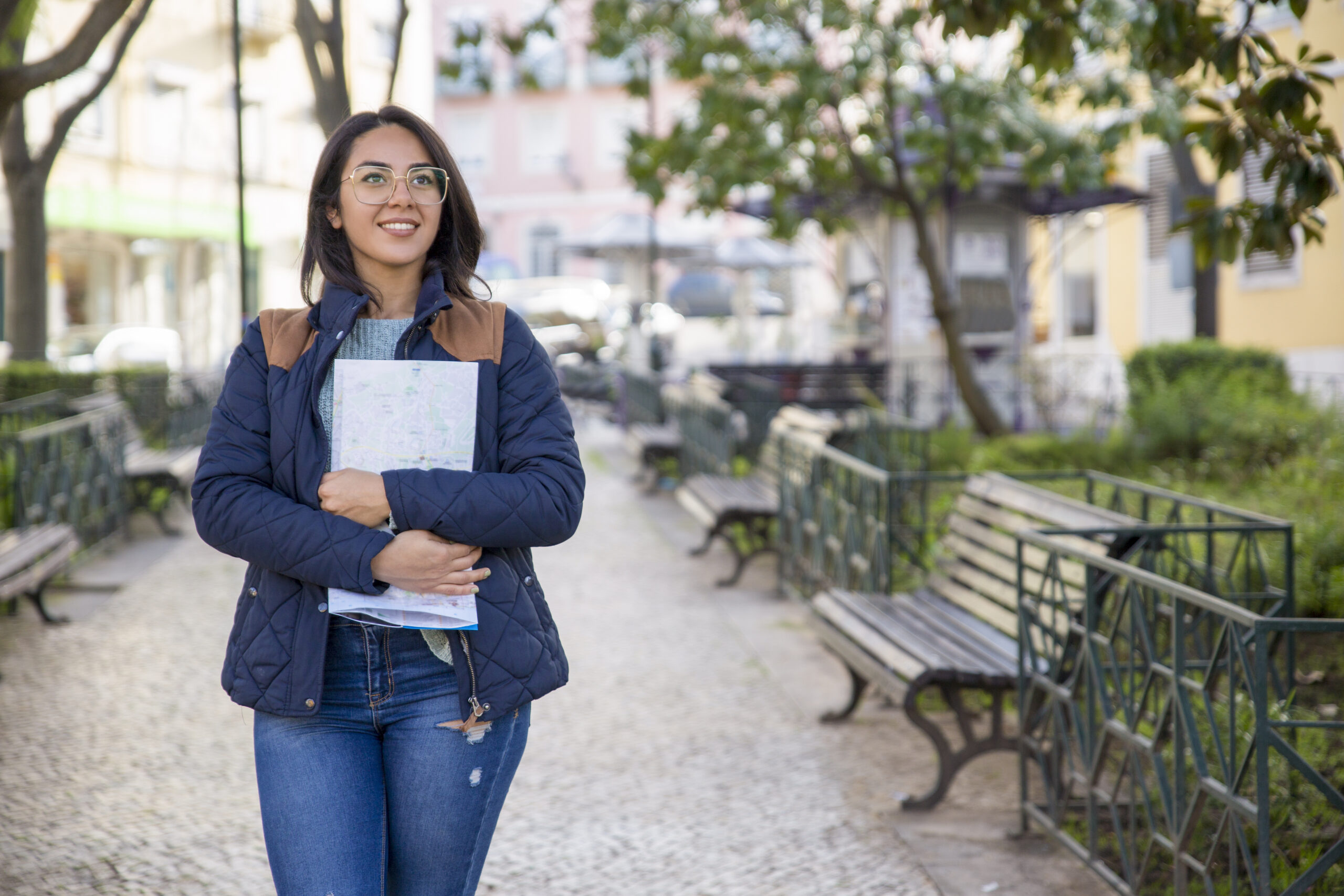 Mulher caminhando na praça com livros na mão e mochila nas costas